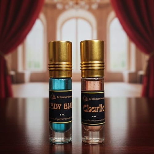 Two perfume bottles with gold caps on a wooden surface, with a blurred background of red curtains and a chandelier.
